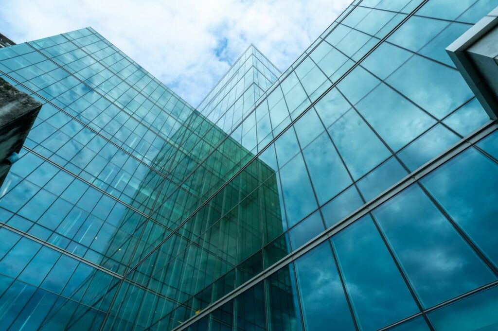 Fachada de prédio comercial com estrutura de vidro refletindo o céu azul, símbolo do mercado imobiliário corporativo.