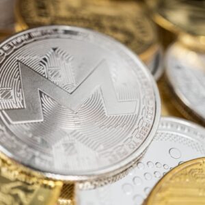 Moeda física de Monero em destaque sobre outras criptomoedas douradas, representando ativos digitais alternativos.