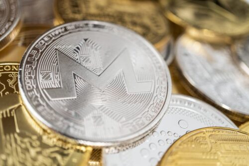 Moeda física de Monero em destaque sobre outras criptomoedas douradas, representando ativos digitais alternativos.