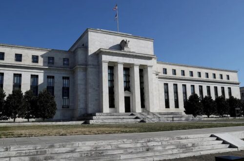 Fachada do Federal Reserve, banco central dos EUA, em Washington, com colunas e bandeira americana.