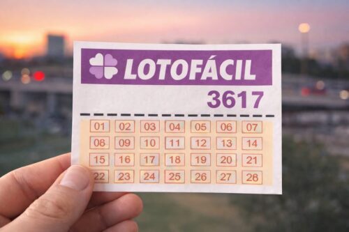 Bilhete da Lotofácil 3617 segurado em primeiro plano, com cidade ao entardecer desfocada ao fundo.