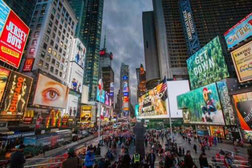 Vista da Times Square à noite, com prédios altos, painéis luminosos, multidão de pedestres e tráfego intenso no centro de Nova York.
