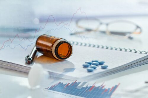 Frasco de medicamento e comprimidos sobre relatório com gráficos, simbolizando debate sobre patente farmacêutica e mercado.