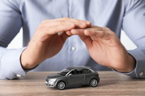 Mãos protegendo miniatura de carro sobre mesa, conceito de seguro de carro e proteção financeira.
