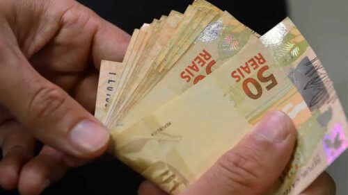 Mãos segurando cédulas de R$50 ilustram o valor do salário mínimo 2026 e o impacto no poder de compra.