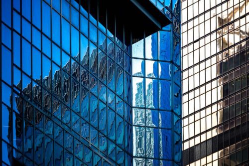 Fachada de prédio corporativo com fachada de vidro refletindo outros edifícios no centro financeiro.