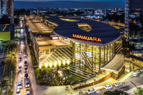 Vista aérea noturna do Manauara Shopping, em Manaus, um dos ativos estratégicos do portfólio da Allos (ALOS3). A imagem destaca a fachada iluminada e a moderna arquitetura do empreendimento urbano.