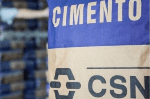 Detalhe de um saco de cimento da marca CSN, com o logotipo da empresa em destaque e outros sacos empilhados ao fundo.