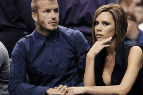 David e Victoria Beckham sentados juntos em um evento, de mãos dadas.