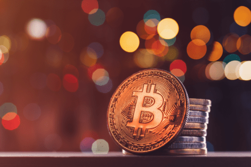 Imagem de moedas de bitcoin empilhadas, simbolizando investimentos em criptomoedas, com fundo colorido de luzes difusas, representando o mercado de criptografia.