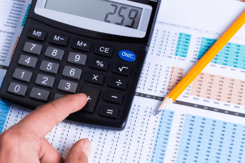 Pessoa usando calculadora e analisando planilhas financeiras.