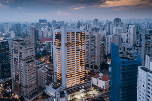 Imagem de uma vista aérea de um centro urbano com prédios modernos e altos ao pôr do sol, destacando-se um edifício residencial iluminado na cidade.