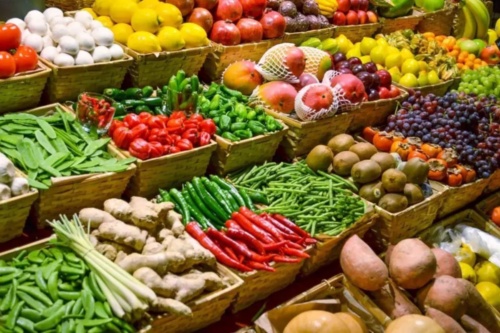 Bancada de feira com cestos de vime repletos de frutas, legumes e hortaliças variadas, representando a variação de preços de alimentos que compõe os índices de inflação.