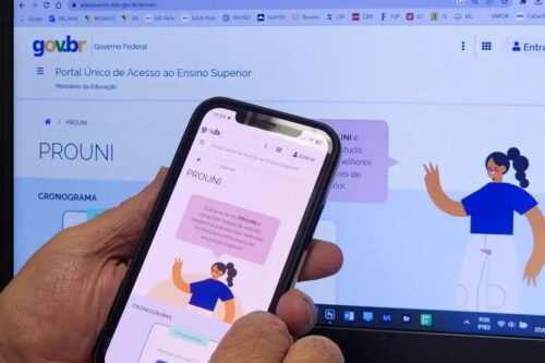 Uma pessoa segura um smartphone em primeiro plano, exibindo a página oficial do Prouni (Programa Universidade para Todos) no site do Governo Federal brasileiro (gov.br).