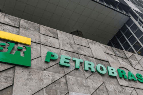 Vista inferior da fachada de concreto da sede da Petrobras (Edise). Na parede de textura geométrica triangular, destacam-se as letras verdes em relevo formando o nome "PETROBRAS" e parte do logotipo "BR" em verde e amarelo acima. A parte superior mostra detalhes das janelas de vidro do edifício.