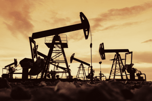 Imagem de uma operação de extração de petróleo com plataformas e perfuradoras ao pôr do sol, destacando a exploração de petróleo e gás natural.