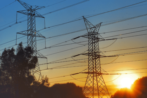 Linhas de energia contra o nascer do sol em um ambiente rural.