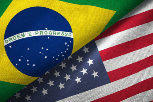 Composição em close-up mostrando as bandeiras do Brasil e dos Estados Unidos unidas diagonalmente. A bandeira brasileira aparece na parte superior esquerda e a norte-americana na parte inferior direita. O tecido apresenta uma textura visível e dobras suaves, criando um efeito de profundidade e intersecção entre as duas nações.