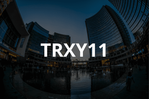 O ticker TRXY11 escrito em letras brancas centralizadas sobre uma foto noturna de arquitetura moderna, mostrando prédios espelhados curvados ao redor de uma praça com fontes de água iluminadas.