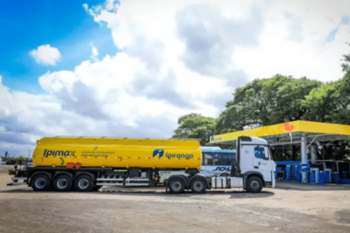 Caminhão tanque amarelo da linha Ipimax estacionado em um posto de combustível Ipiranga, com foco na logística de distribuição de combustíveis.