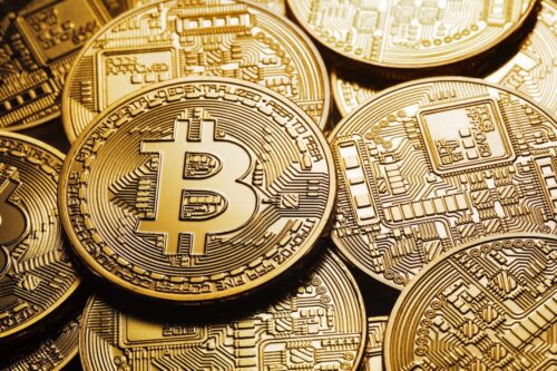 Moedas de Bitcoin douradas empilhadas e espalhadas sobre superfície escura.