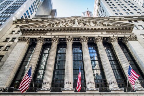 Fachada da Bolsa de Nova York com bandeiras dos EUA, simbolizando queda dos mercados e tensão global.