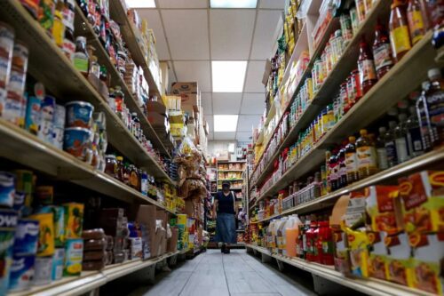 Corredor de mercado com prateleiras cheias, ilustrando IGP-10 e aumento de preços do atacado em alimentos e produtos básicos