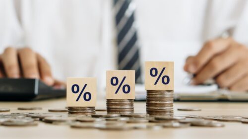 Pilha de moedas com símbolos de porcentagem indica alta dos juros e impacto da inflação no mercado financeiro.