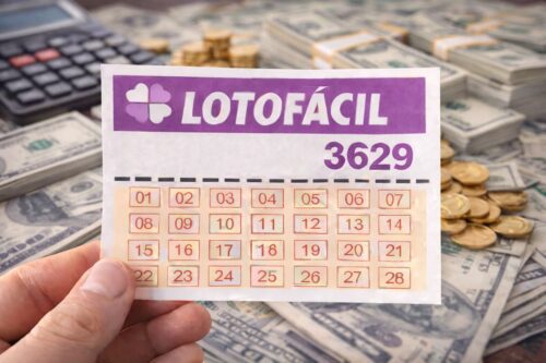 Bilhete da Lotofácil 3629 segurado por mão com pilhas de dinheiro, moedas e calculadora ao fundo, simbolizando prêmio da loteria