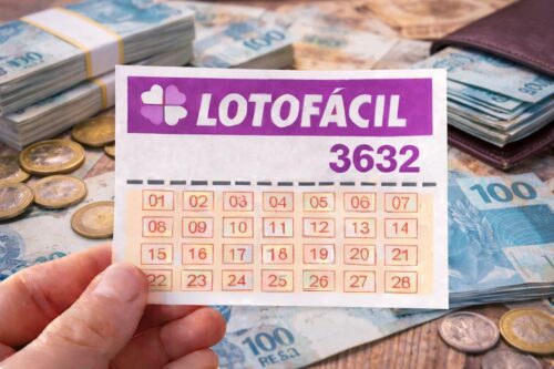 Bilhete da Lotofácil 3632 segurado por mão sobre mesa com notas de real e moedas, representando prêmio da loteria.