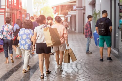 Pessoas caminhando com sacolas em área comercial em dia de movimento, ilustrando onde é feriado em 19 de março.
