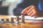 ão empilhando moedas em pilhas crescentes sobre mesa, representando planejamento financeiro e investimentos.