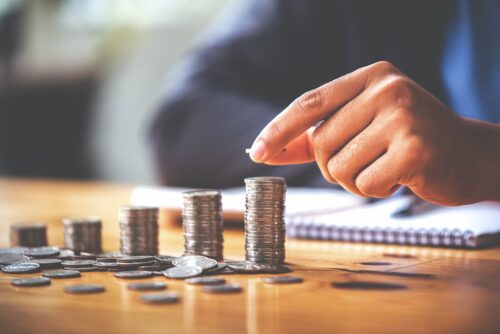 ão empilhando moedas em pilhas crescentes sobre mesa, representando planejamento financeiro e investimentos.
