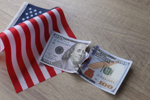 Bandeira dos EUA com nota de 100 dólares rasgada, simbolizando impacto econômico após payroll negativo e perda de 92 mil empregos.