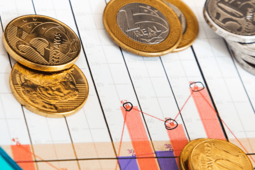 Imagem de moedas de euro sobre gráfico financeiro com análise de investimentos, destacando crescimento econômico e planejamento financeiro.
