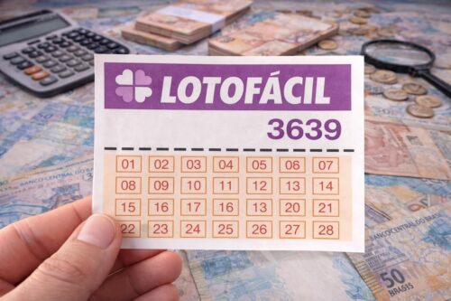 Cartela de aposta do jogo de loteria Lotofácil 3639, sobre uma mesa com dinheiro, calculadora e lupa ao fundo.