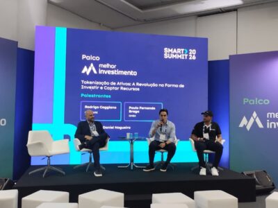 Painel de negócios no Smart Summit 2026 com três palestrantes debatendo investimentos em palco diante do público.