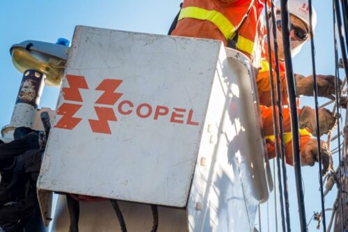 Dois técnicos da Copel trabalham na manutenção da rede elétrica em um dia ensolarado.