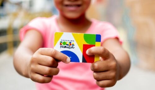 Criança segura cartão do Bolsa Família em destaque, representando pagamento do benefício social no Brasil.