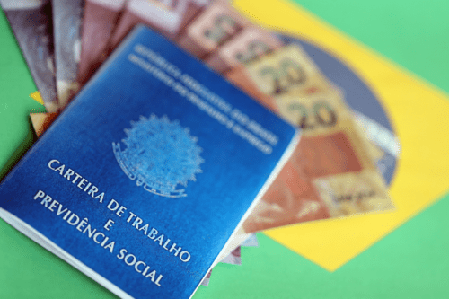 Carteira de trabalho brasileira e livro azul da previdência social e notas de dinheiro em reais na bandeira.