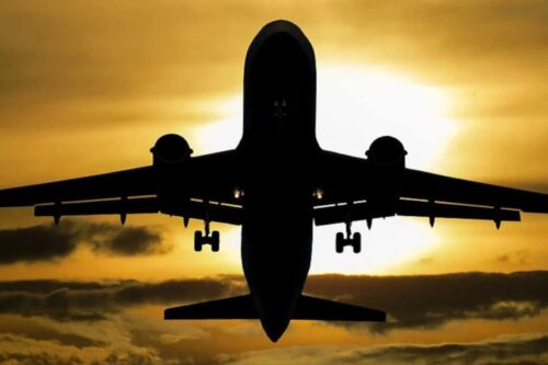 Silhueta de um avião comercial de grande porte decolando ou pousando contra um pôr do sol vibrante.