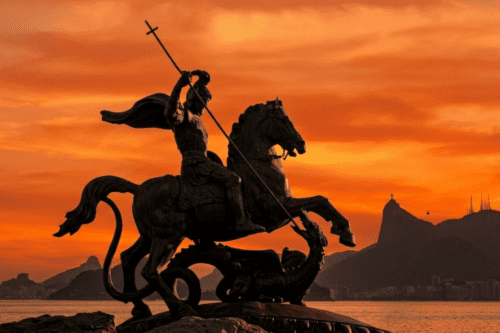 Estátua de São Jorge montado em um cavalo, com o céu ao entardecer ao fundo, representando força e proteção na cultura brasileira.