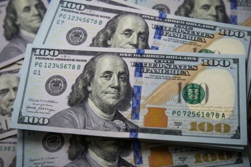Várias notas de 100 dólares americanos (Benjamin Franklin) espalhadas e sobrepostas.