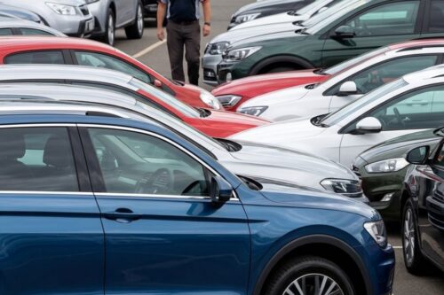 Diversos carros de diferentes cores e modelos estacionados em fileiras em um pátio de revenda.