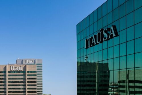 achada de um prédio moderno espelhado em tons de azul e verde com o logotipo da Itaúsa em destaque.