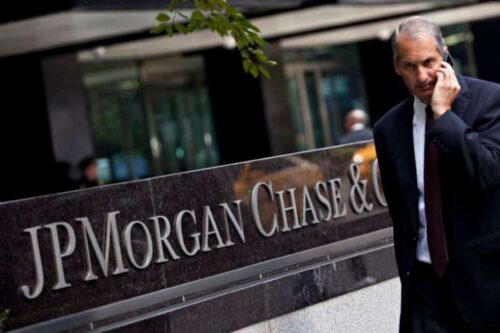 Um homem de terno escuro e camisa branca caminha em frente à sede do banco JPMorgan Chase & Co.