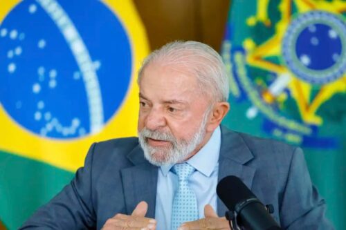 O presidente Luiz Inácio Lula da Silva falando em um microfone durante uma transmissão ou entrevista.