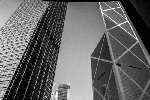 Imagem de prédios altos e modernos no centro de uma cidade, mostrando uma arquitetura contemporânea com estruturas de vidro e iluminação urbana ao entardecer.