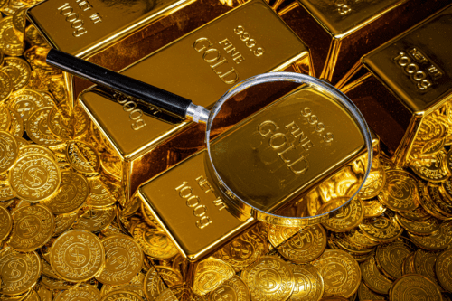 Imagem de barras de ouro, moedas de ouro e uma lupa, simbolizando riqueza e valor financeiro