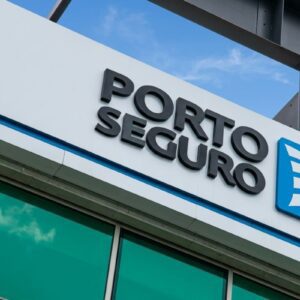 Fachada em ângulo de um prédio moderno exibindo o logotipo da Porto Seguro. O letreiro possui letras pretas em relevo ao lado de um ícone azul quadrado com listras brancas curvadas.